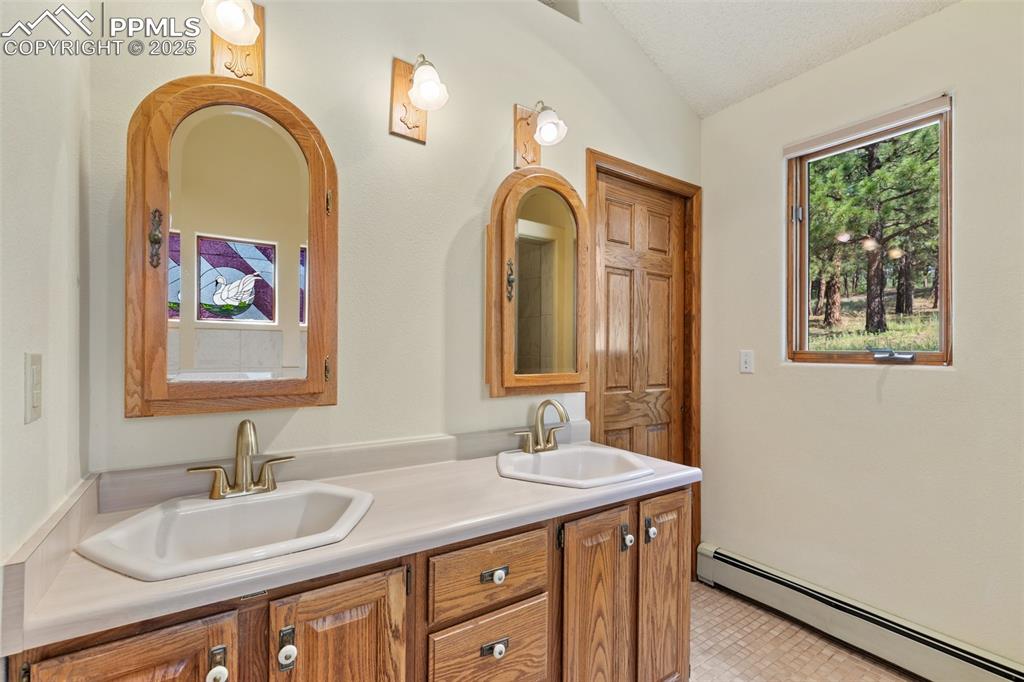Image 40 of 50: Bathroom featuring a baseboard heating unit, double vanity, vaulted ceiling