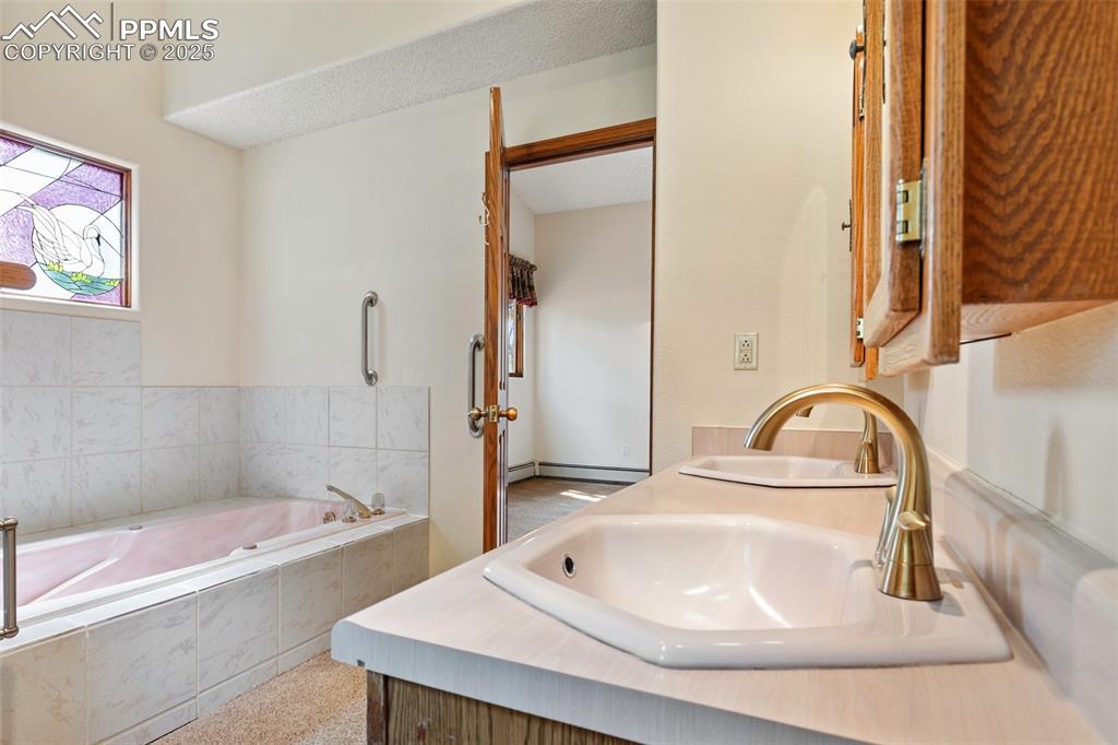 Image 42 of 50: Bathroom with a garden tub, double vanity, and a baseboard radiator