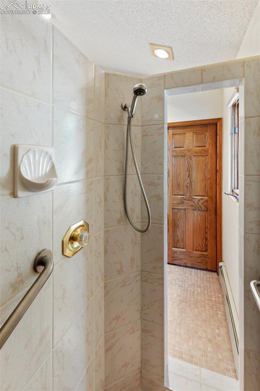 Image 43 of 50: Full bath with a tile shower, a textured ceiling, and baseboard heating