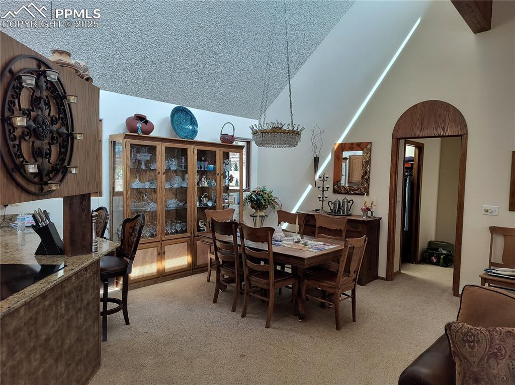 Image 9 of 50: Dining room featuring light colored carpet, a textured ceiling, vaulted cei