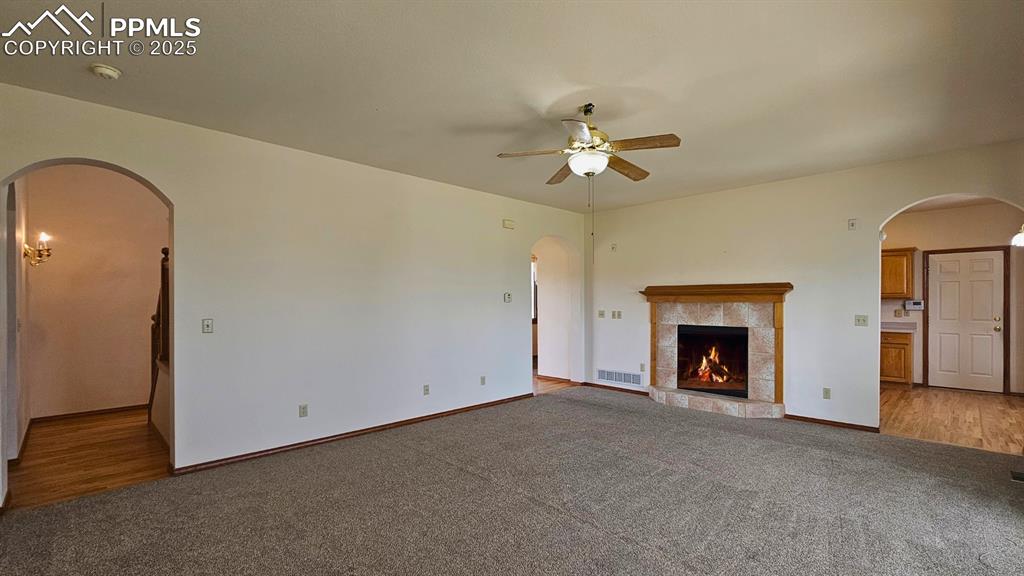 Image 10 of 28: Unfurnished living room featuring ceiling fan, light carpet, a tiled firepl