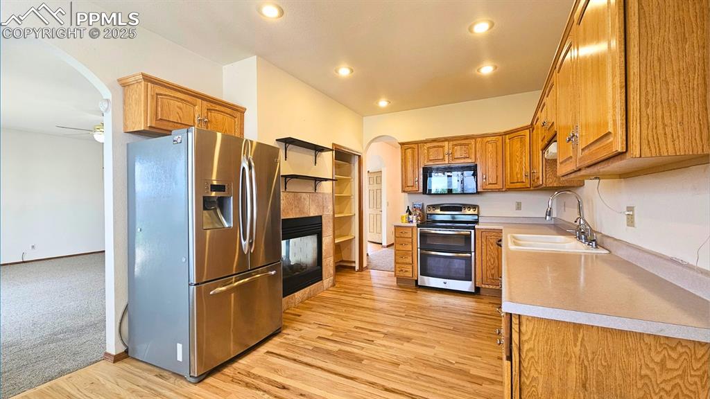 Image 5 of 28: Kitchen featuring stainless steel appliances, arched walkways, brown cabine