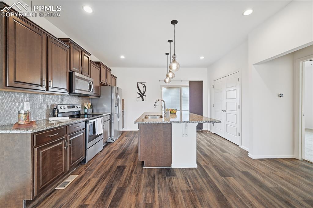 Image 11 of 40: Kitchen with light stone counters, stainless steel appliances, dark wood fi