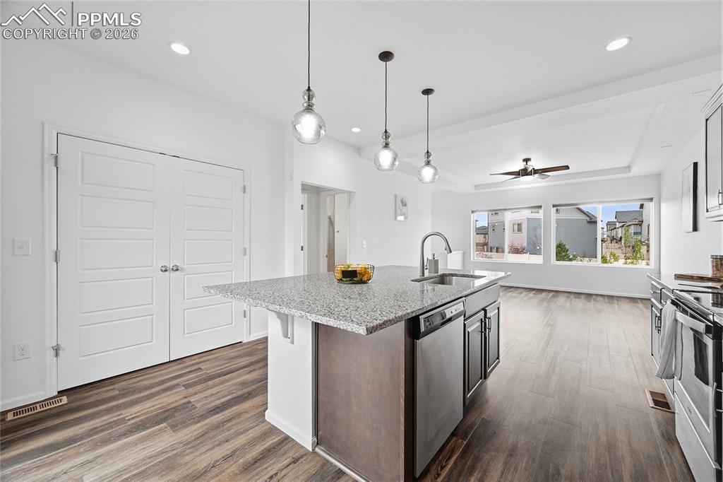 Image 14 of 40: Kitchen with a kitchen island with sink, light stone countertops, hanging l