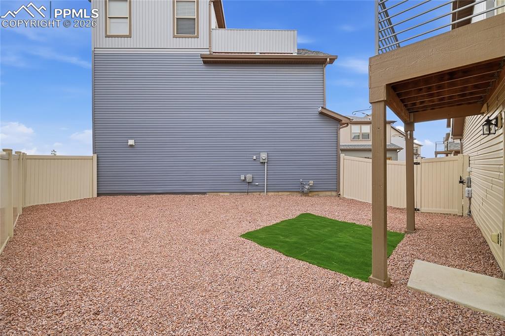 Image 32 of 40: View of fenced backyard featuring a patio area with rocks and turf