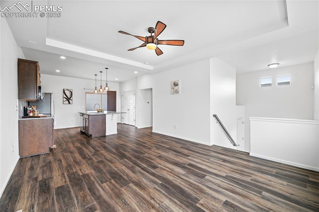 Image 7 of 40: Unfurnished living room featuring a raised ceiling, a ceiling fan, and dark