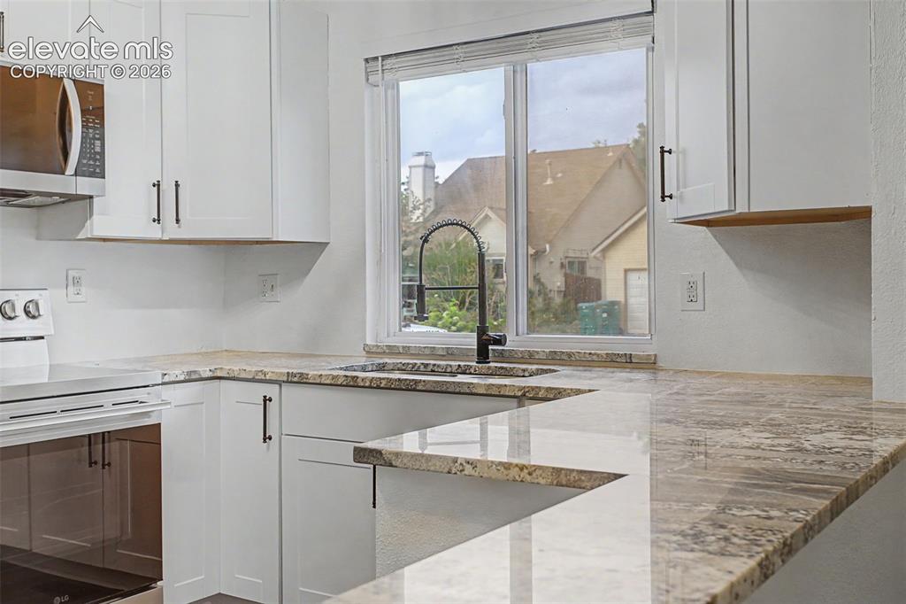 Image 10 of 37: Kitchen featuring white cabinetry with dark hardware, a stainless steel mic