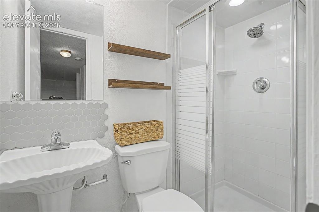 Image 15 of 37: Bathroom featuring a pedestal sink, hex tile backsplash, and a glass-enclos