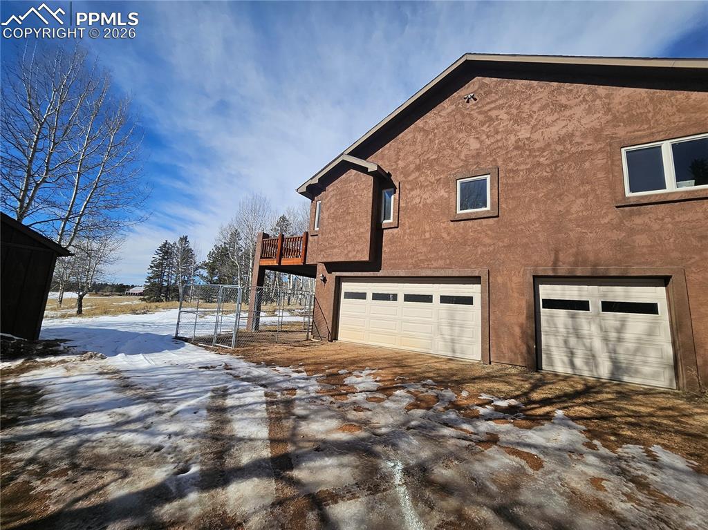 Image 28 of 48: Snow covered gravel driveway with stucco siding, a garage, and a deck - add