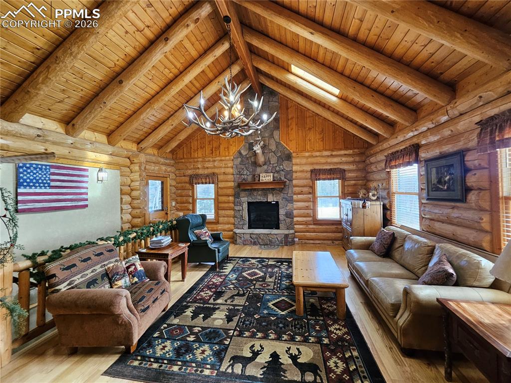 Image 32 of 48: Living area with rustic walls, a high wood beamed ceiling, a deer antler ch