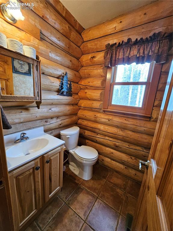 Image 37 of 48: Half bathroom in cabin with vanity and log walls