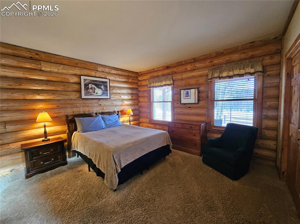 Image 38 of 48: Cabin primary bedroom featuring carpet flooring and rustic log wood walls
