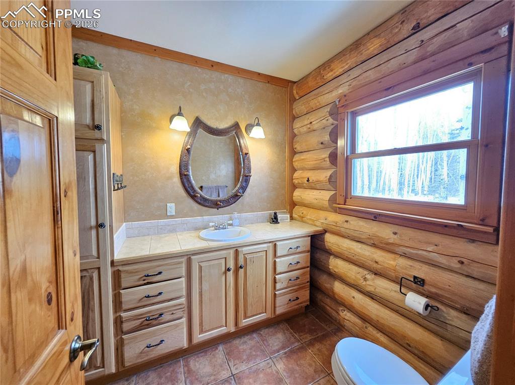 Image 39 of 48: Cabin primary bathroom featuring log walls, vanity, and dark tile patterned