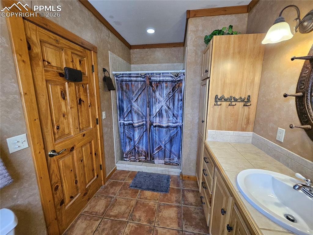 Image 40 of 48: Bathroom featuring a shower stall, vanity, ornamental molding, and dark til
