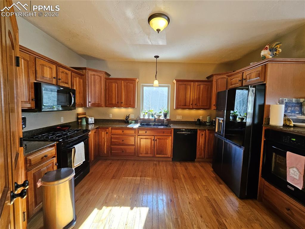 Image 7 of 48: Kitchen with wood finish cabinetry, black appliances, hanging light fixture