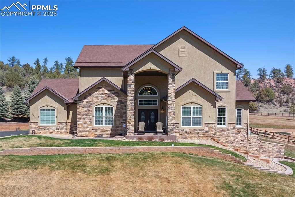 Image 34 of 41: View of front facade with stone siding, stucco siding, a front lawn, and fe