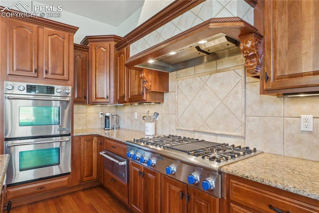 Image 7 of 41: Kitchen featuring light stone countertops, custom range hood, decorative ba