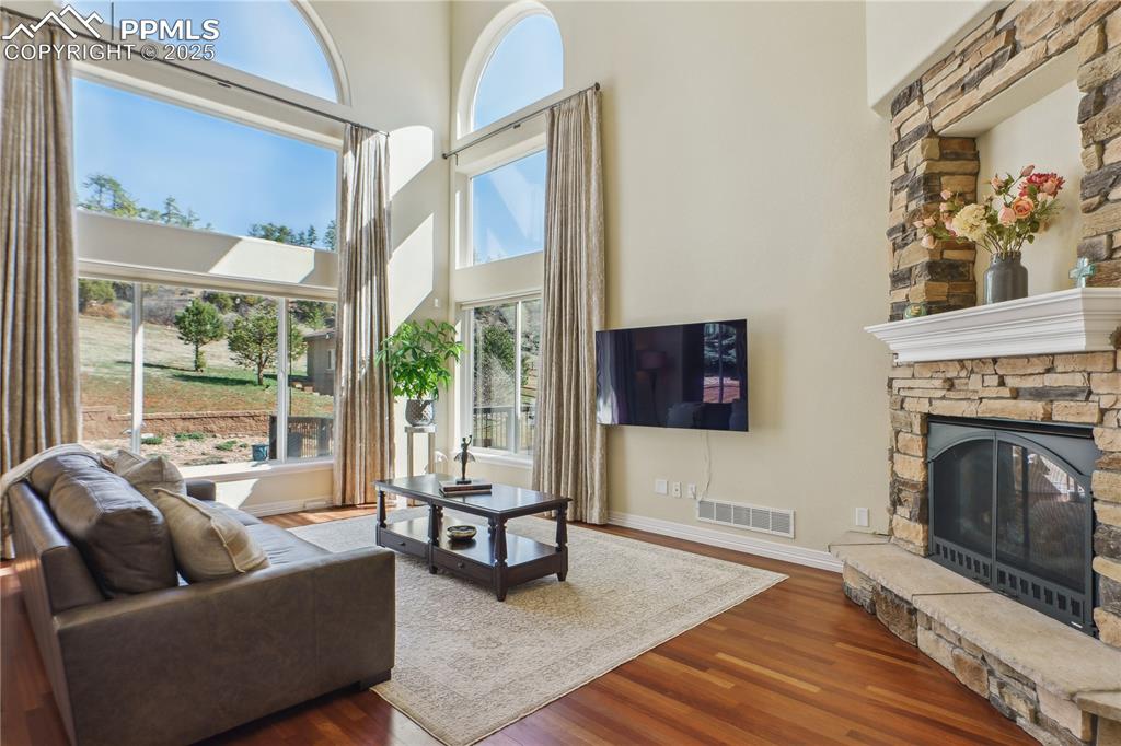 Image 9 of 41: Living area with wood finished floors, visible vents, a fireplace, a high c
