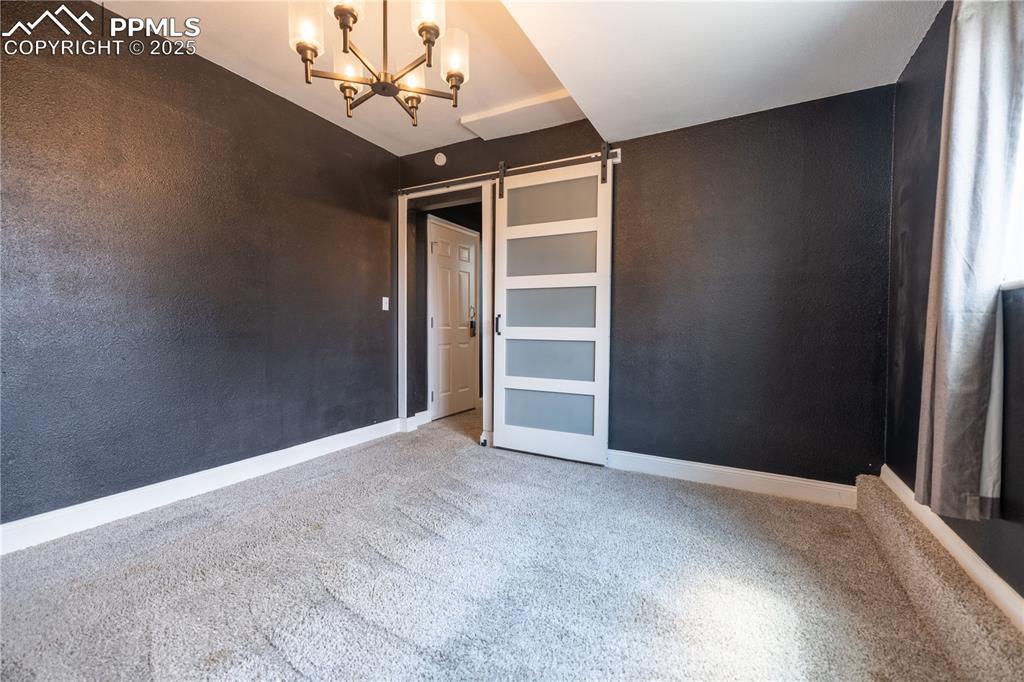 Image 23 of 28: Lower level flex space featuring a barn door, carpet floors, and a chandeli