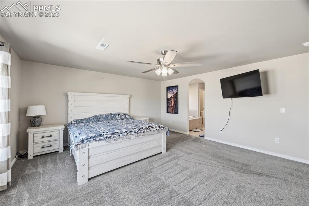 Image 26 of 41: The large Primary Bedroom features neutral carpet, a lighted ceiling fan, 5