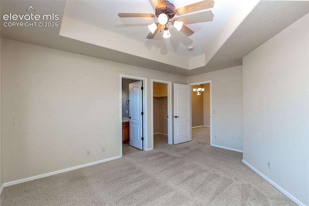 Image 14 of 23: Carpet in primary bedroom with ceiling fan and tray ceilings