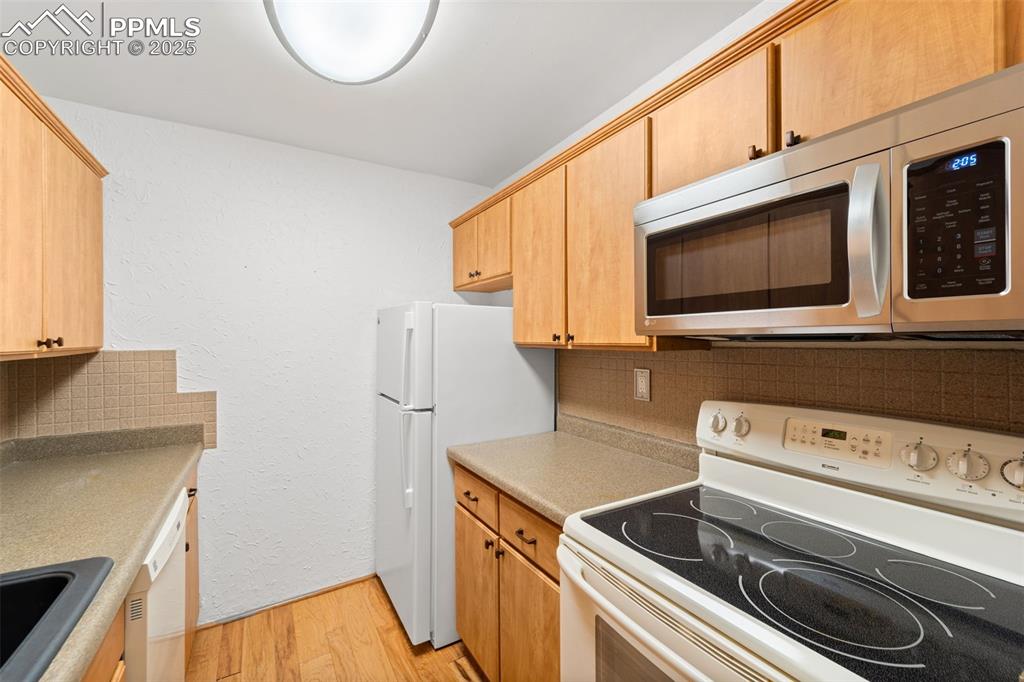 Image 8 of 23: Kitchen with white appliances, light wood-type flooring, tasteful backsplas