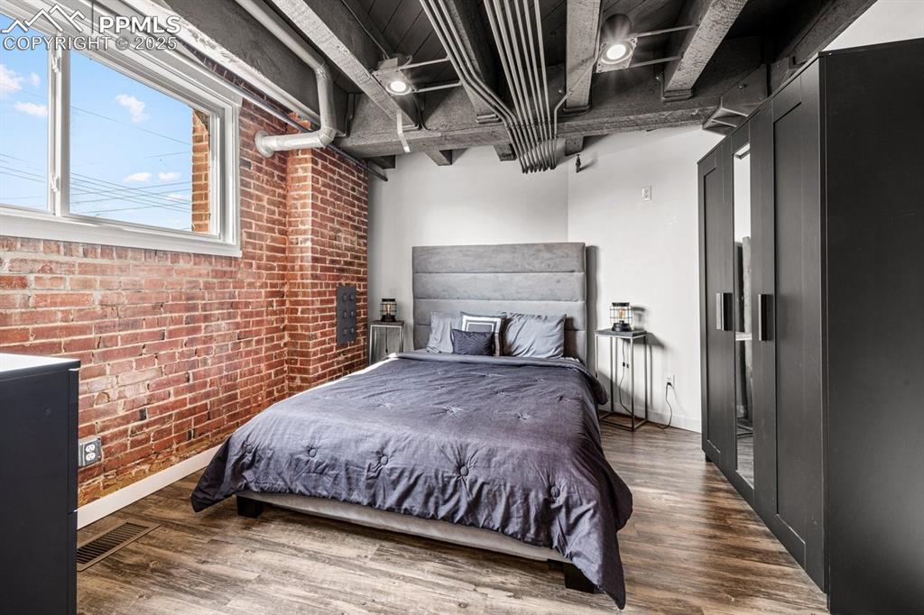Image 21 of 32: Bedroom featuring brick wall and wood finished floors