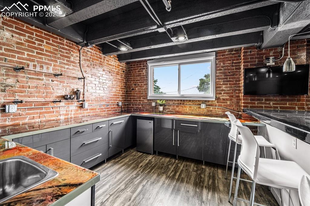 Image 4 of 32: Kitchen with gray cabinets, dark wood-type flooring, brick wall, fridge, an