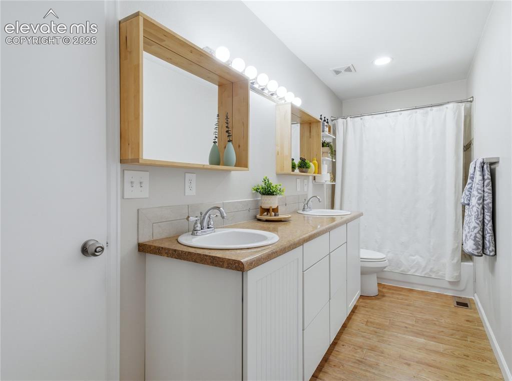 Image 18 of 29: Dual vanity with integrated sinks, wood-finish flooring, and a shower-tub c