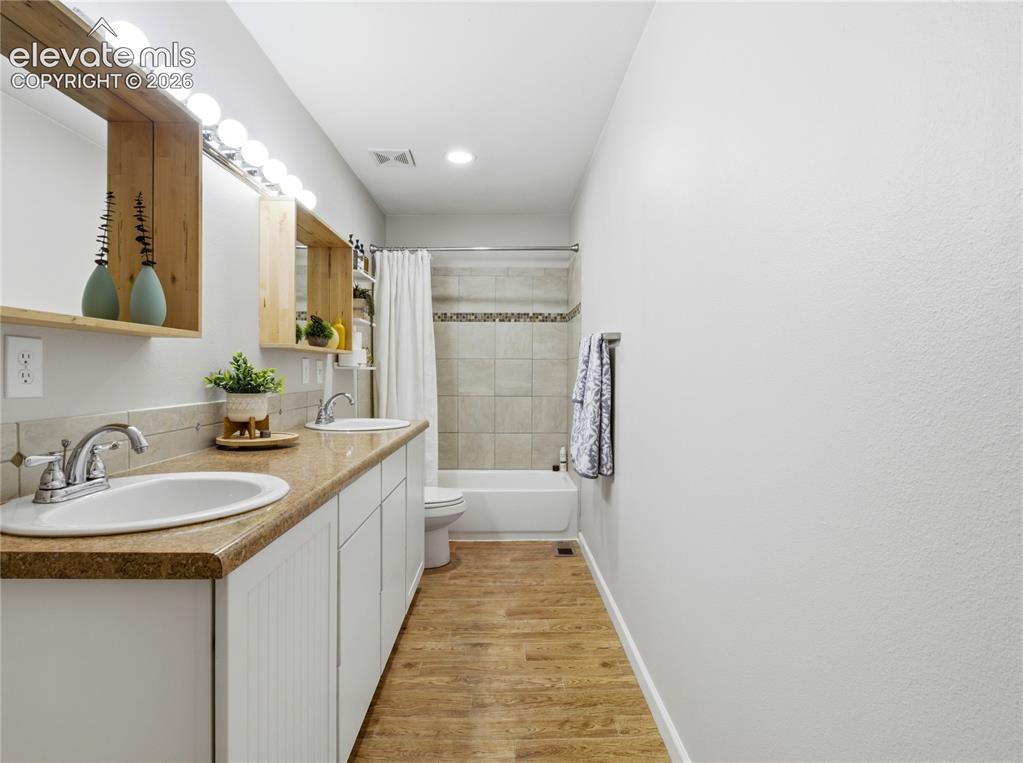 Image 19 of 29: Dual vanity with integrated sinks, wood-finish flooring, tiled shower surro