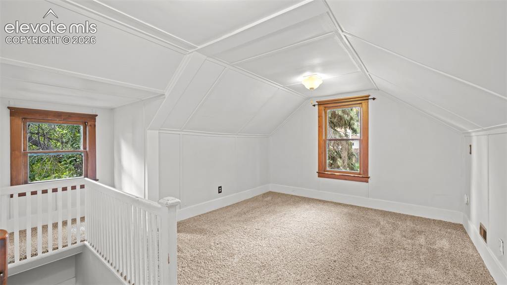 Image 18 of 38: Carpeted room featuring sloped ceilings, white paneling, two windows with w