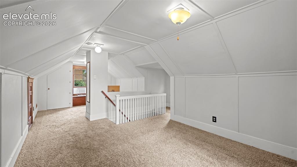 Image 19 of 38: Carpeted room with a pitched ceiling and white paneled walls