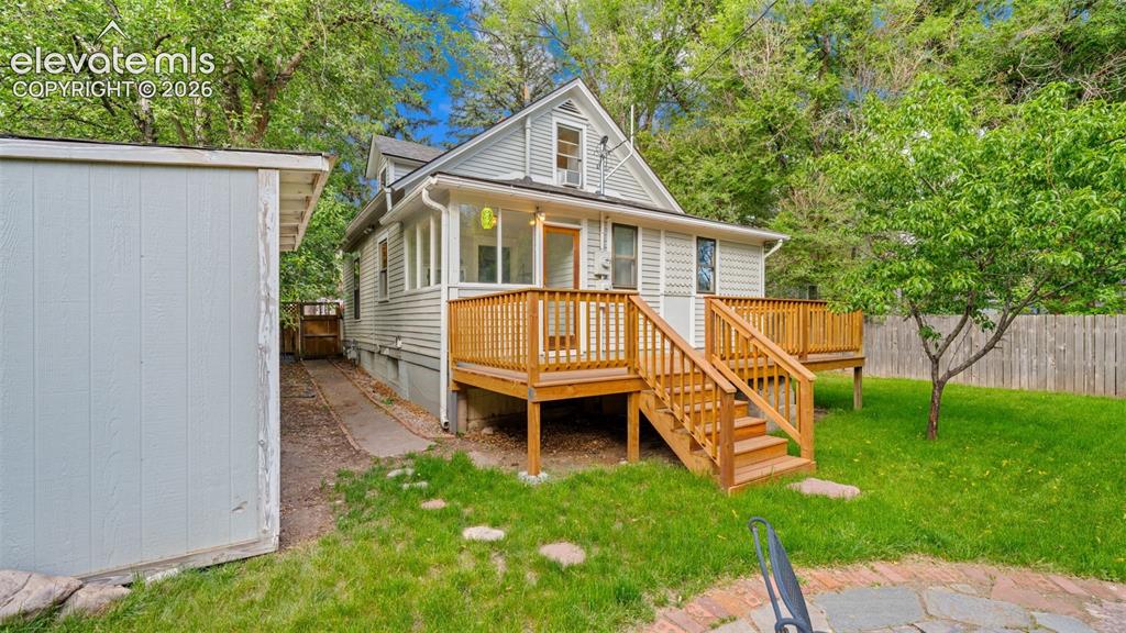 Image 24 of 38: Rear exterior with a spacious wood deck and staircase descending to a stone