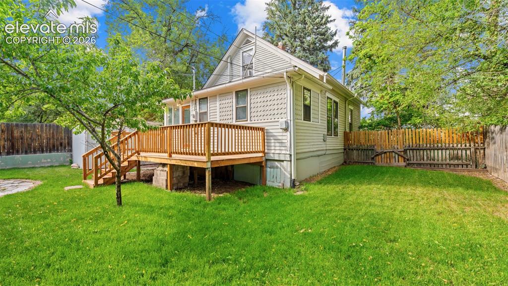 Image 25 of 38: Expansive green lawn with a multi-level wooden deck featuring railing and s