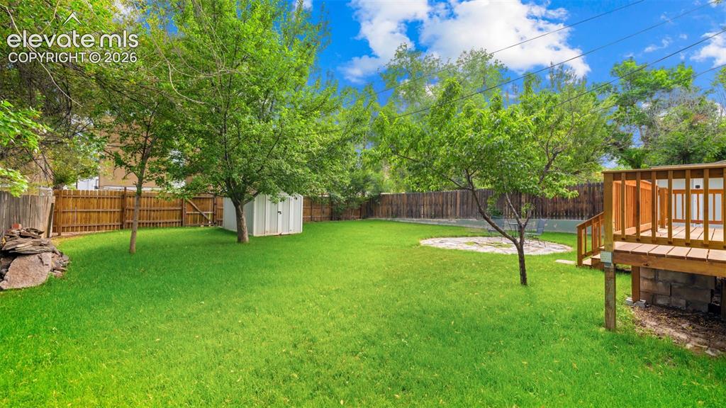Image 26 of 38: Spacious backyard featuring a wooden privacy fence, mature trees, a storage