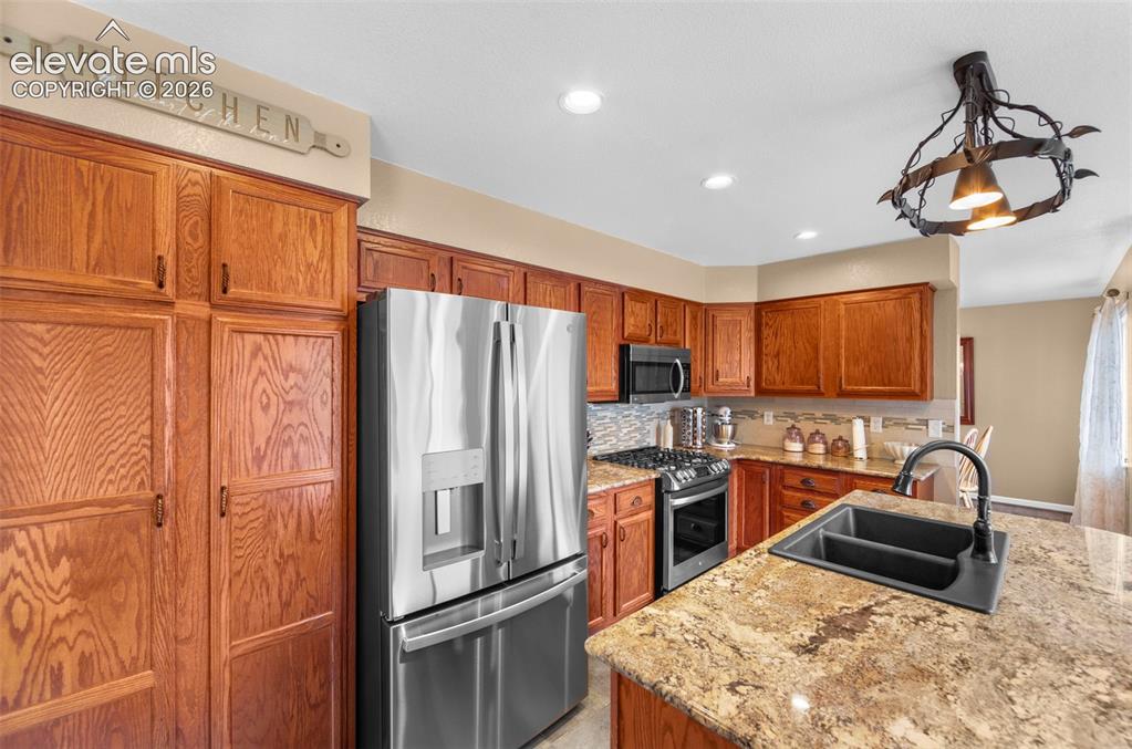 Image 11 of 41: Kitchen featuring wood cabinetry, stainless steel appliances, granite count