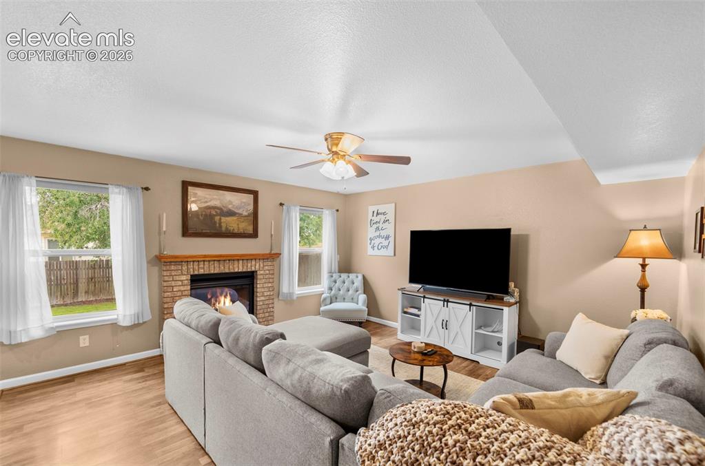 Image 13 of 41: Living area featuring a brick fireplace with a wood mantle, wood-finish flo