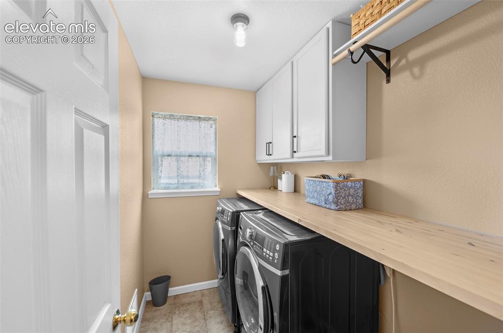 Image 16 of 41: Dedicated laundry area featuring a wood-finish countertop, white cabinetry,