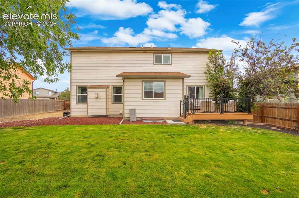 Image 27 of 41: Expansive green lawn with a composite deck, black metal railings, and priva