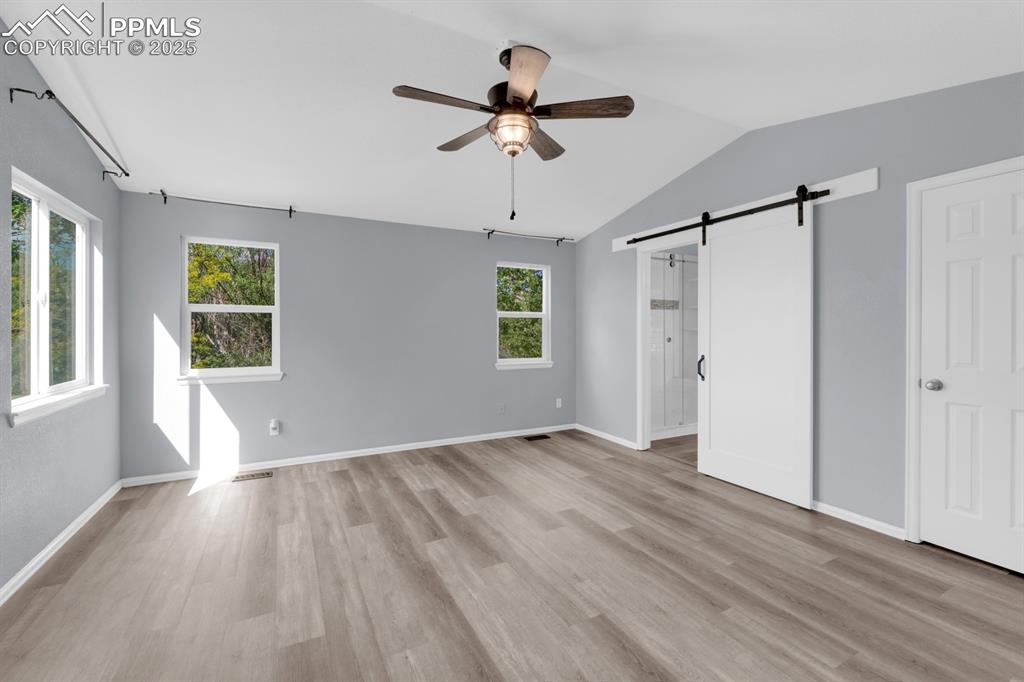 Image 12 of 36: Master bedroom with a barn door, vaulted ceiling, ensuite bath, and a ceili