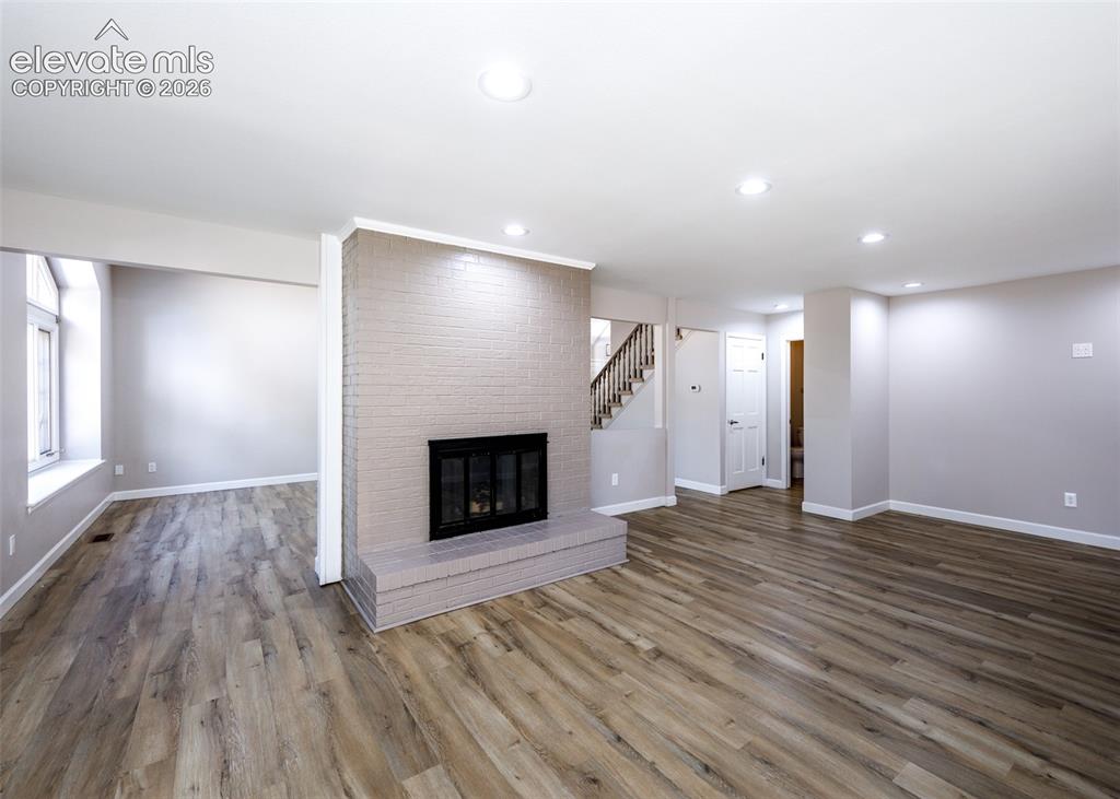 Image 13 of 44: Expansive living area featuring wood-finish flooring, a painted brick firep