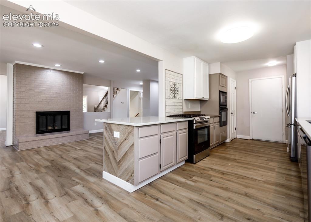 Image 19 of 44: Expansive wood-finish flooring throughout, complemented by a brick fireplac