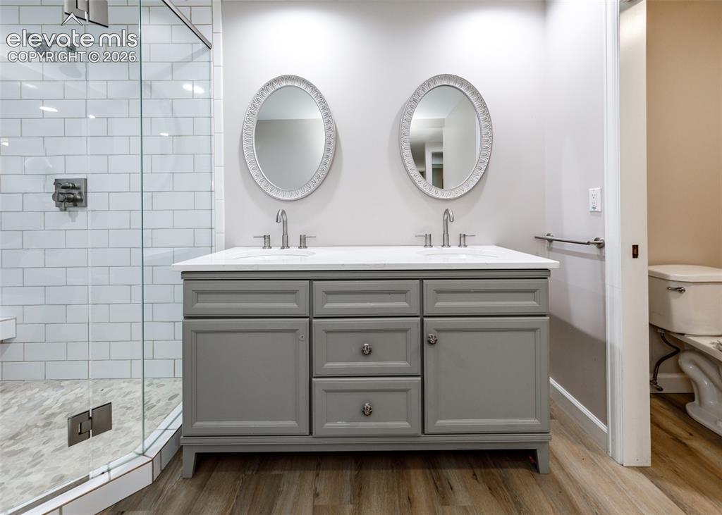 Image 29 of 44: Dual vanity with a white countertop and gray cabinetry, surrounded by wood-