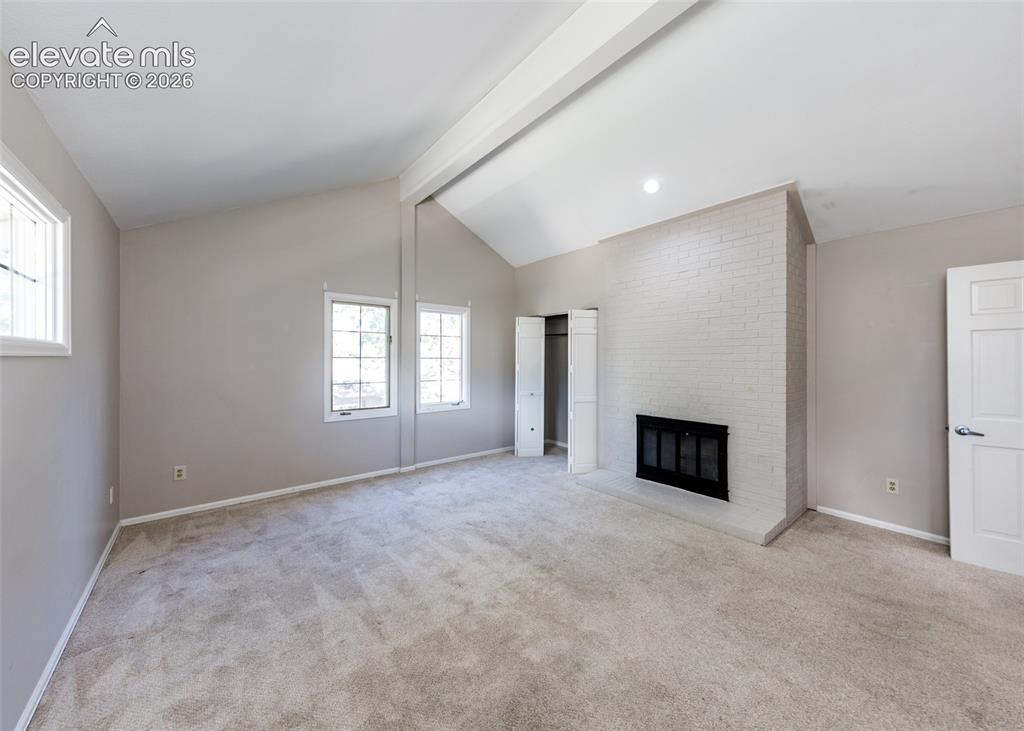 Image 32 of 44: Vaulted ceiling with an exposed beam, white brick fireplace, and light-tone