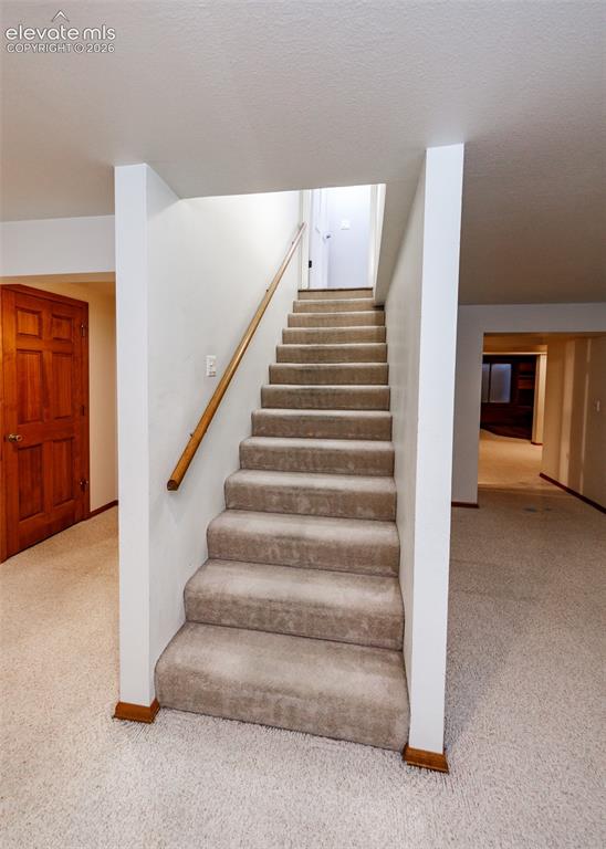 Image 40 of 50: Carpeted staircase with a wood-finish handrail, surrounded by neutral wall