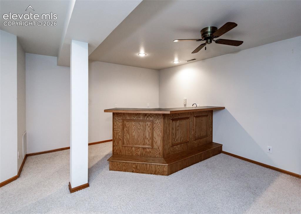 Image 42 of 44: Built-in wood-paneled bar with a dark countertop, recessed lighting, and a 