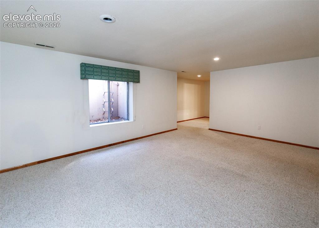 Image 42 of 50: Expansive carpeted room with white walls, a window with a green valance, an