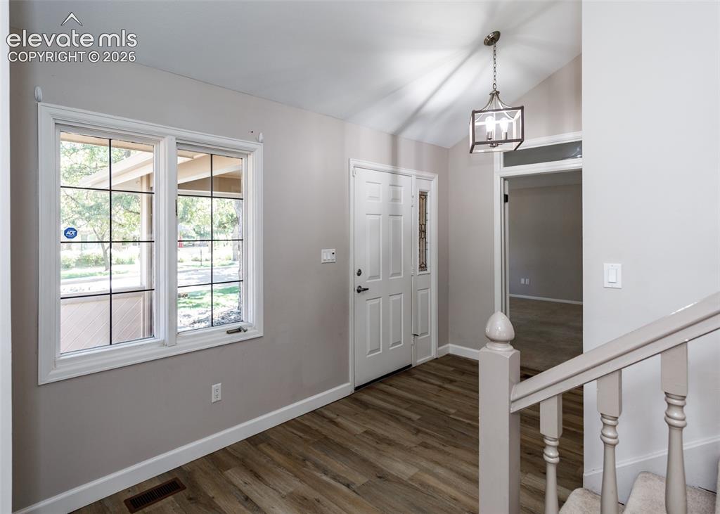 Image 6 of 50: Vaulted entry with wood-finish flooring, white paneled entry door, and a de