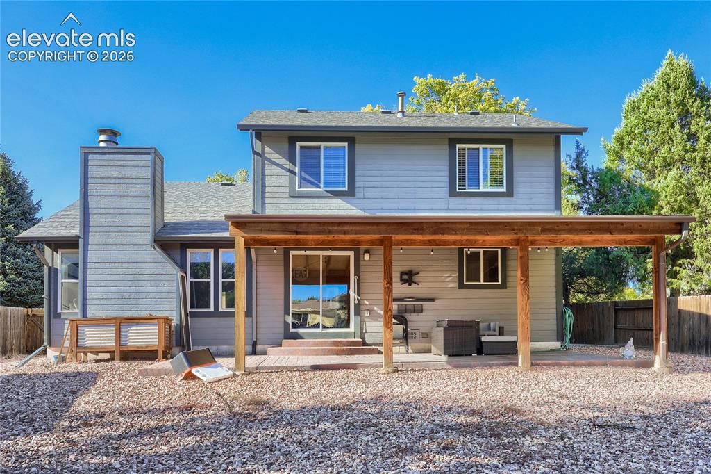Image 16 of 19: Expansive gravel backyard featuring a covered patio with a wood beam struct