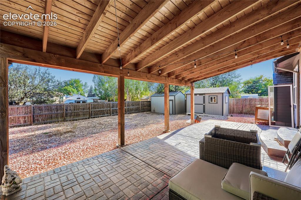 Image 19 of 19: Expansive covered patio with exposed wood ceiling beams and string lighting